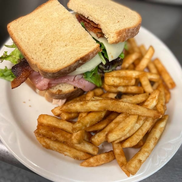 A ShoeBooties Cafe sandwich with bacon, ham, cheese, and lettuce, served with golden fries.