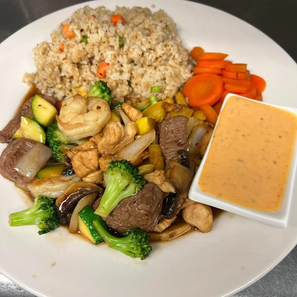 A Southern-style hibachi plate with fried rice, mixed vegetables, shrimp, beef, chicken, and a side of sauce.