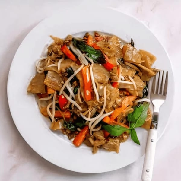 A plate of southern-style noodles with vegetables, bean sprouts, and a fork on a white surface.