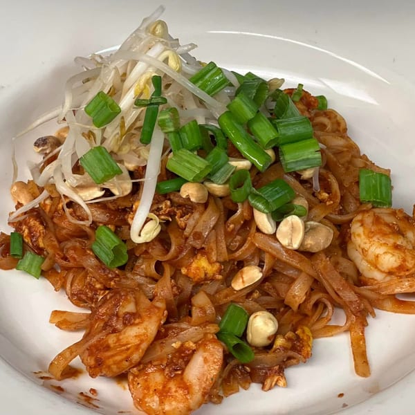 Shrimp Pad Thai with bean sprouts, peanuts, and green onions on a white plate.