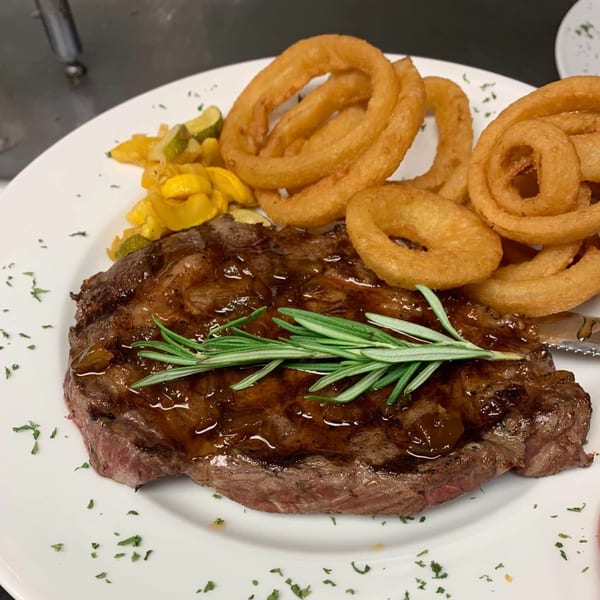 Southern-style steak with gravy, rosemary, onion rings, and sautéed squash on a white plate.