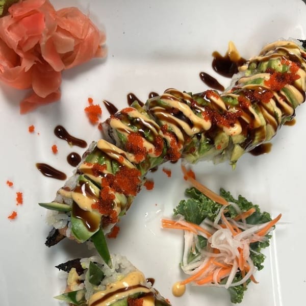 Dragon roll sushi with avocado, roe, and sauces, served with pickled ginger and a side salad.